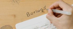 Hand writing the word boring on a desk