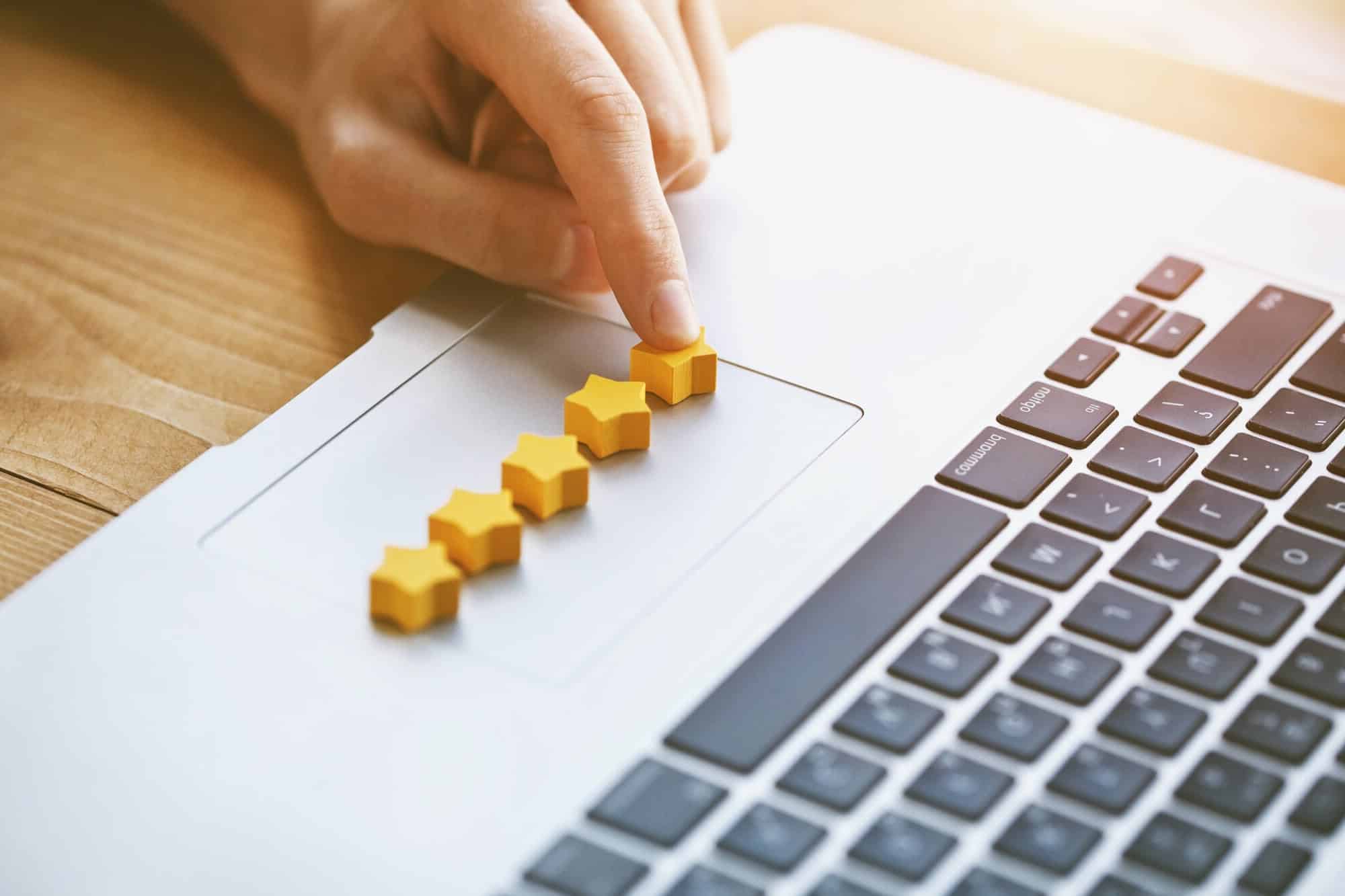 A hand putting yellow stars on their laptop trackpad to represent reviews